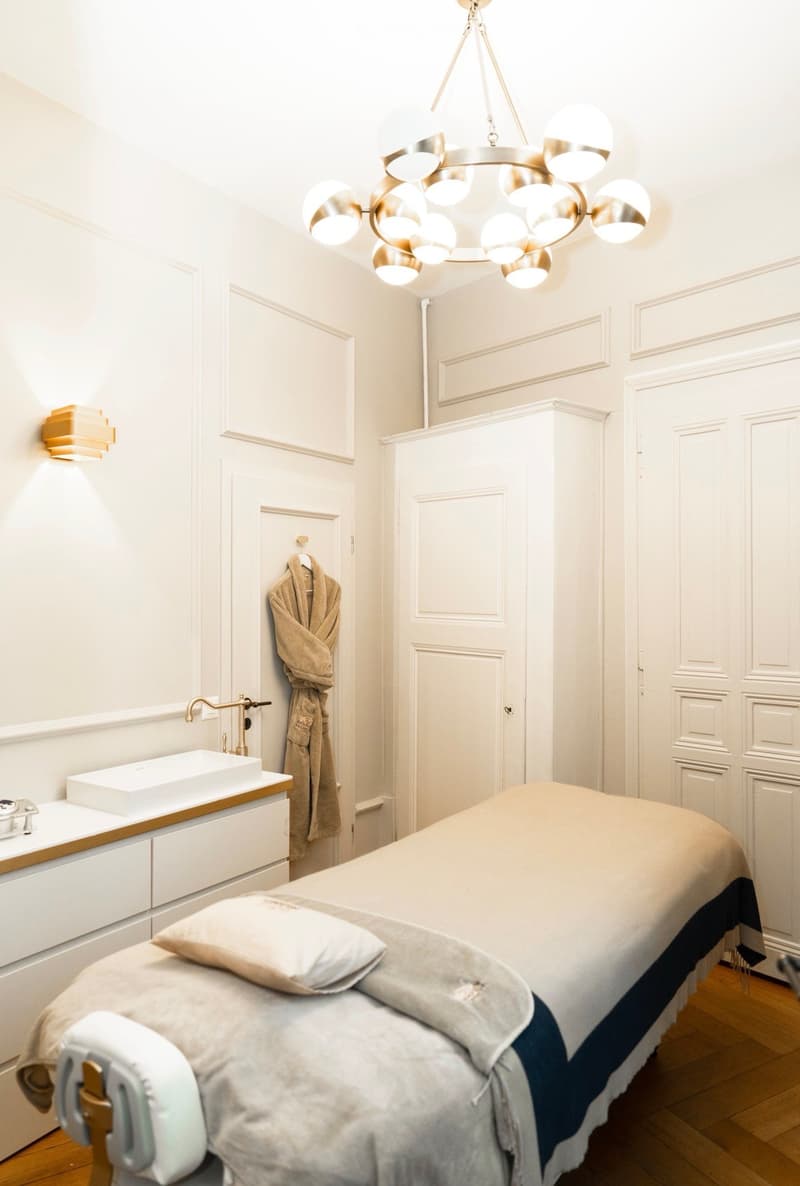 modern massage room with white walls, white cabinets, massage bed, sink, and white cabinets with drawers