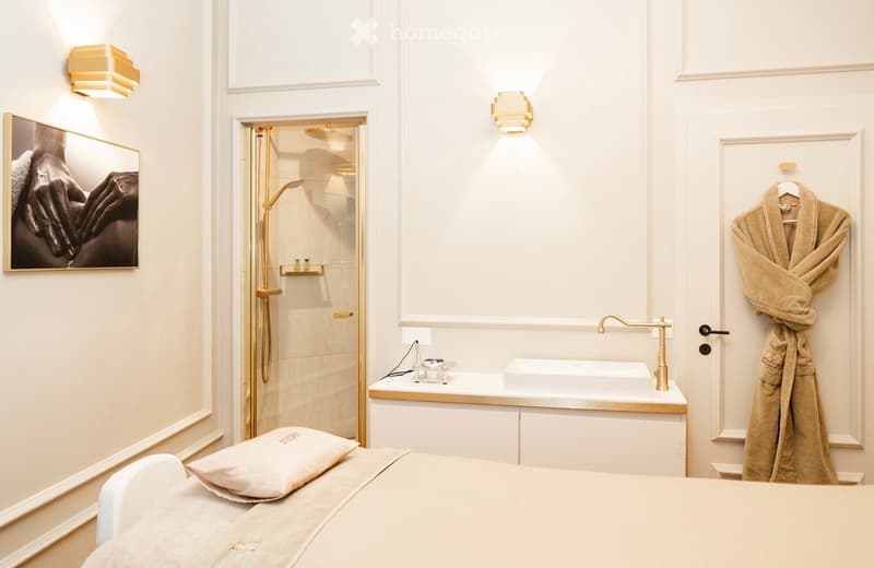 modern bathroom with white walls, white bath, golden fixtures, a shower, bed and a towel