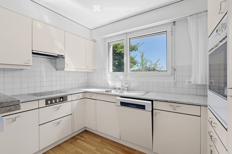 Modern kitchen with white cabinets, granite countertops, a sink, a dishwasher, and a stove. The room features wooden flooring and large windows with white curtains.
