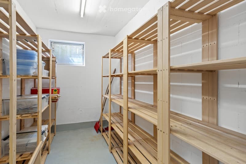 A storage room with multiple wooden shelves filled with storage bins and a broom on the floor.
