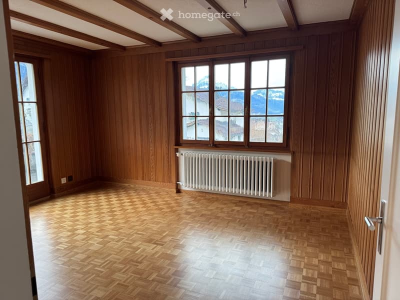 empty room with wooden paneling, wooden parquet flooring, large window with view, radiator