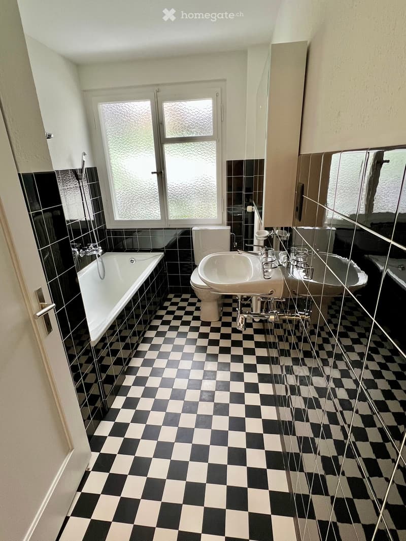 a bathroom with black and white tiled floor, bathtub, white ceramic sink, toilet, and glass window