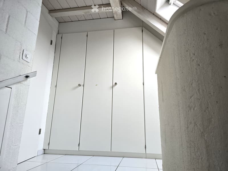 A corner room with white tiled floor, wooden beams on the ceiling and tall white built-in wardrobes