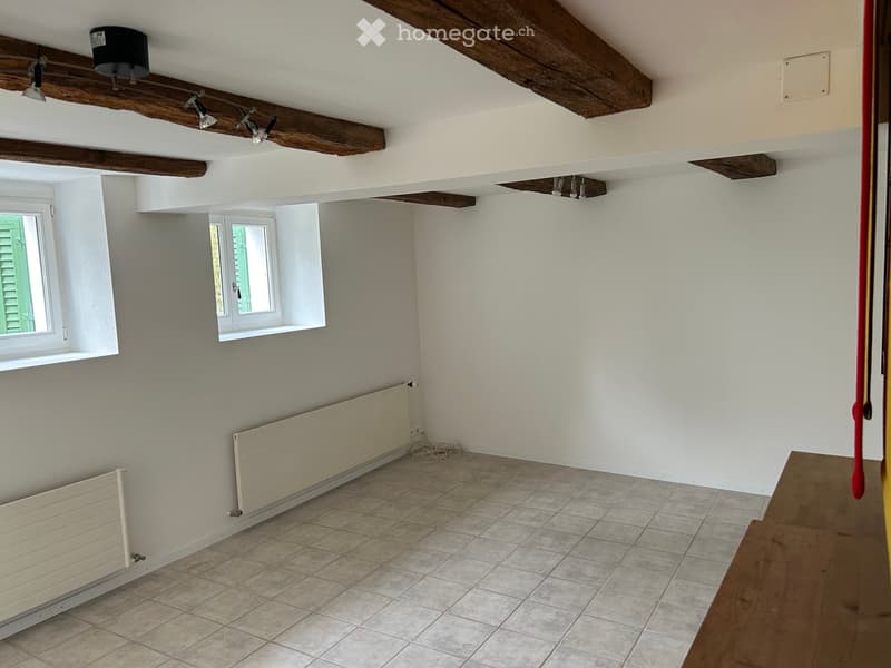 empty room with exposed wooden beams, radiators, two windows, tiled floor, wooden table