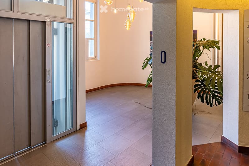 Raised ground floor, tiled flooring, modern elevator, white walls, pendant lights, potted plant, windows, door with number 0