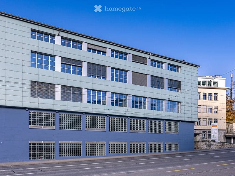 A modern blue building with glass windows and a small balcony on the top floor