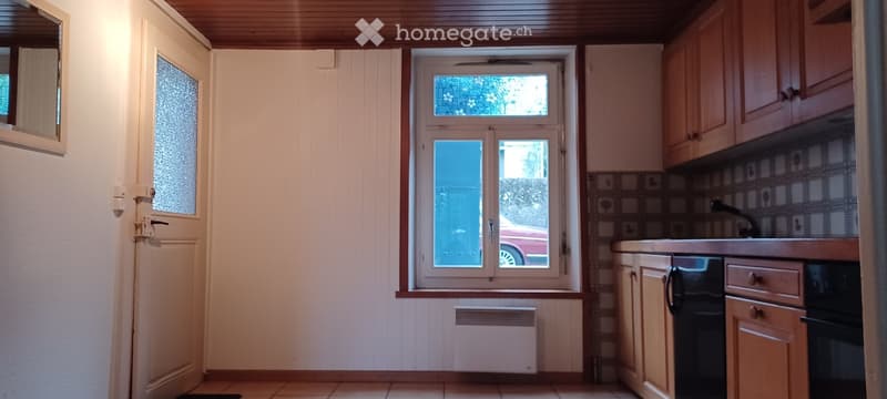 empty kitchen with tiled floor, white walls, wooden cabinets, a window, and a small heater below the window