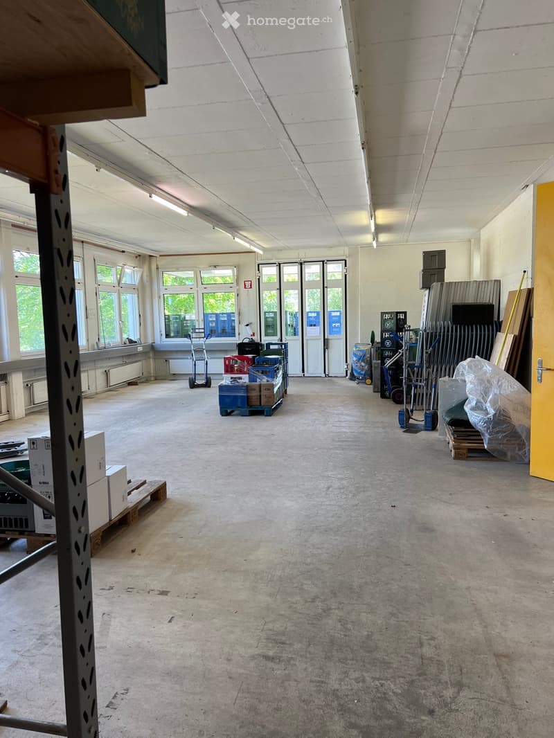 Empty room with concrete floor, large windows, and scattered storage items including boxes, pallets, and a scooter.