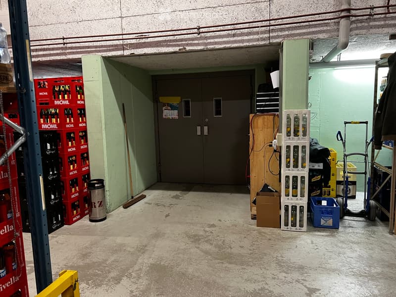 Empty storage area with concrete floor, metal shelving, and a closed door at the end.