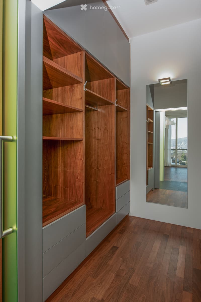 walk-in closet with wooden shelving and drawers, mirrored door, tiled floor, white walls, overhead lighting