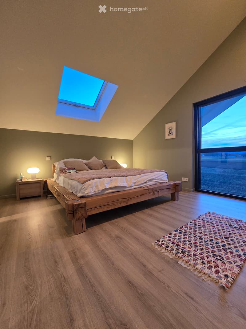 Modern bedroom with a wooden bed, wooden floor, skylight, nightstands, lamps, and a view from the large window.
