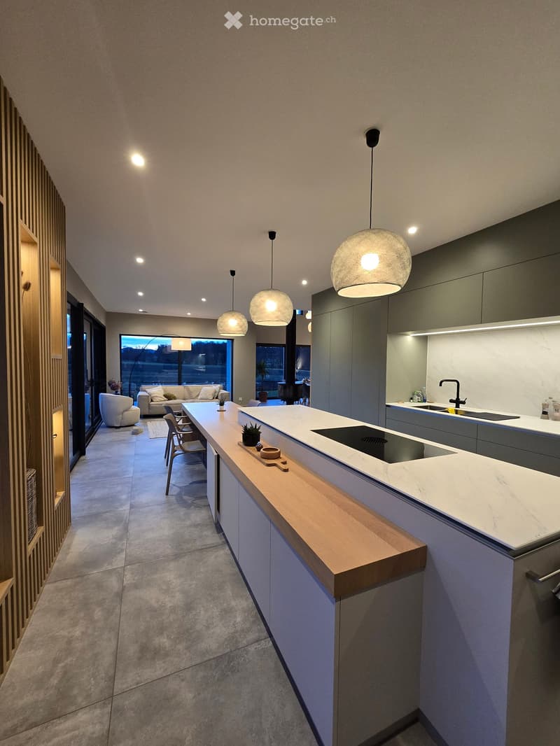 modern kitchen with large marble island, wooden countertops, gas stove, under-cabinet lighting, multiple hanging lights, large windows