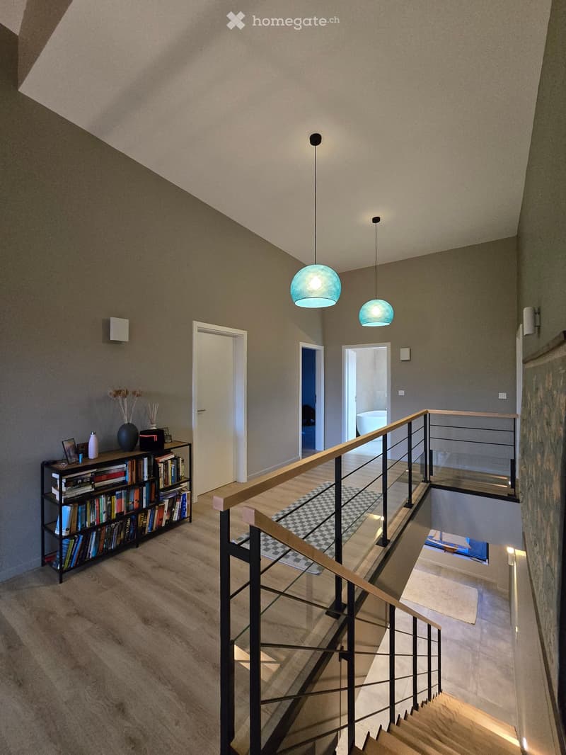 Interior of a house, modern style, wooden floor, open staircase, railings, two lamps, bookshelf with books, entrance door, rooms with furniture visible