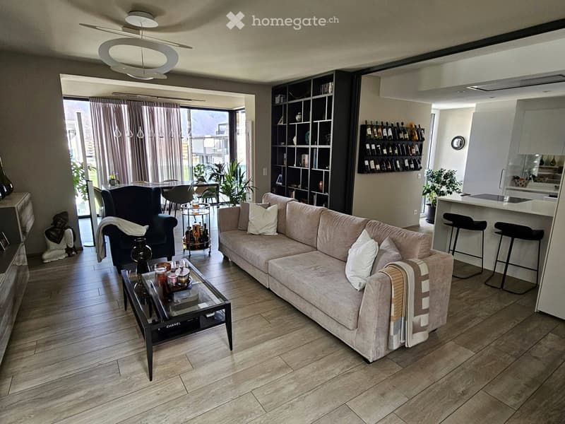 wooden floor, beige couch, coffee table, bookshelf, pendant light, sliding doors, balcony, large windows, kitchen island, bar stools, kitchen