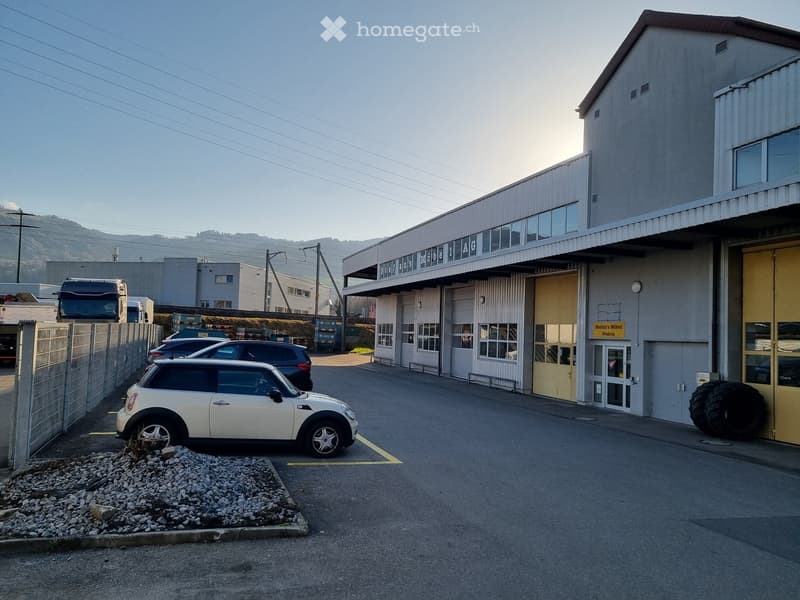 Industrial building with large garage doors, a modern exterior with cars parked in front