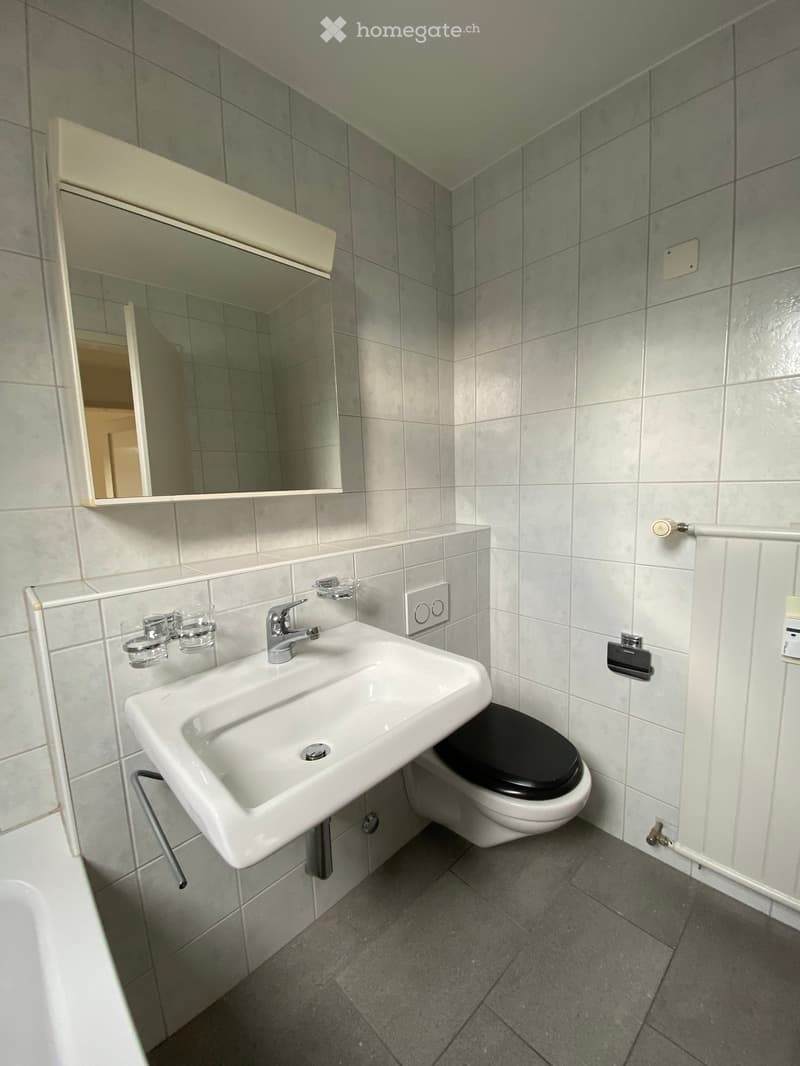 Bathroom: tiled walls, white sink, black toilet, mirror, bathtub, tiled floor