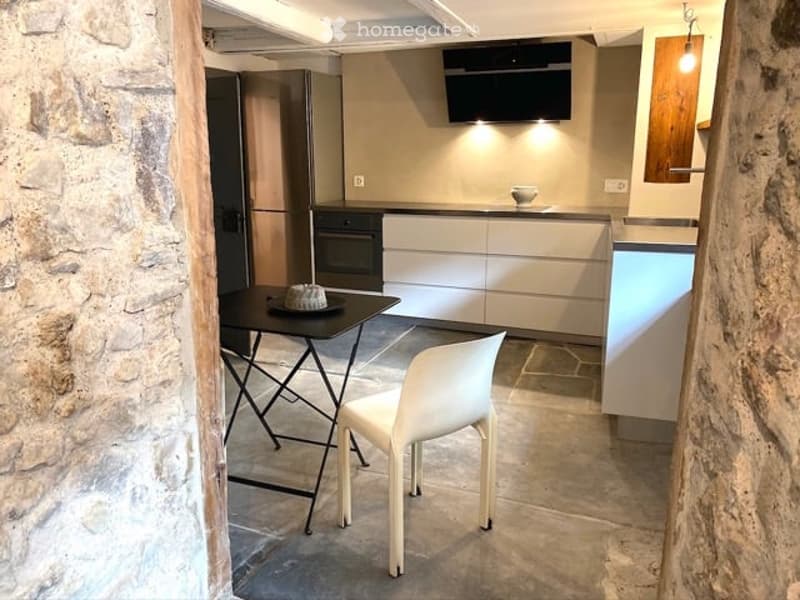 A small dining kitchen with black table, white chair, built-in oven, fridge, and stone wall