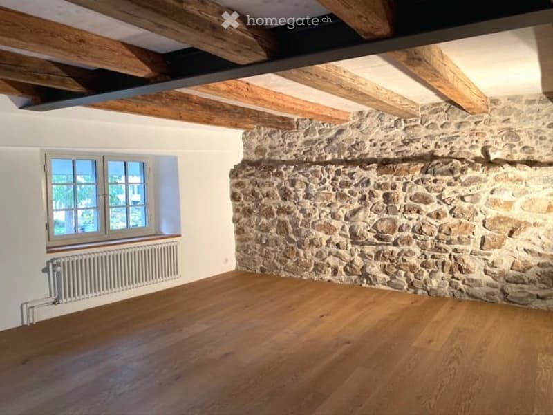 large wooden beam ceiling, hardwood floors, stone wall, single window with a white radiator
