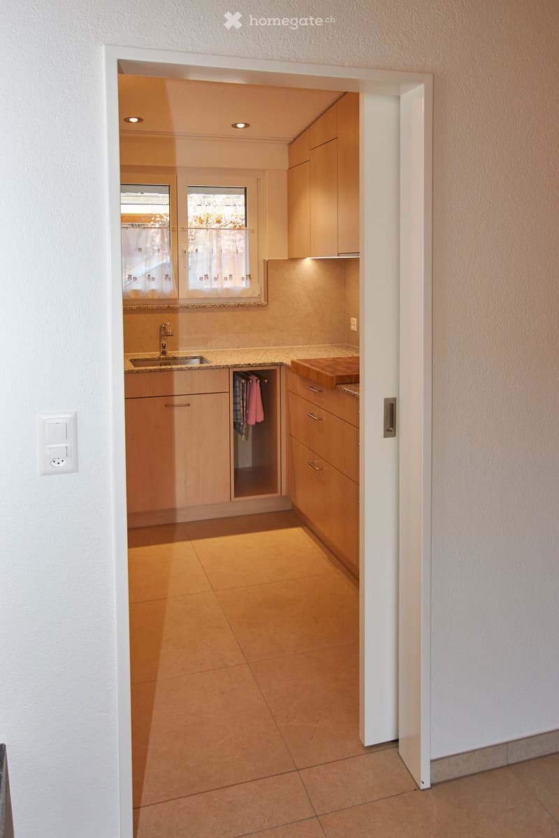 Modern kitchen with wooden cabinets, granite countertops, sink with faucet, dishwasher, electrical outlet, and a view of a window with white curtains.