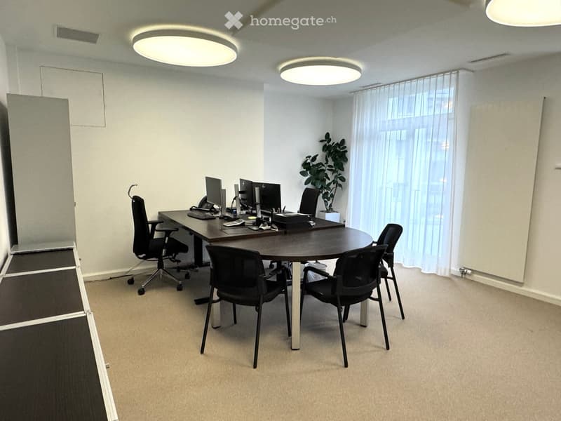 An empty office with a table, chairs, desk, monitors, telephone, computer mouse, keyboards, and potted plants.