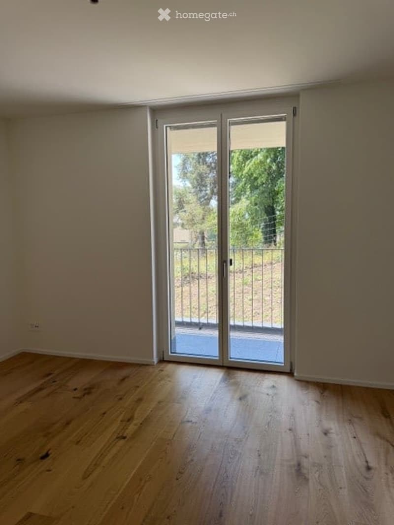 Empty room with wooden flooring and large glass sliding doors leading to an outdoor area.