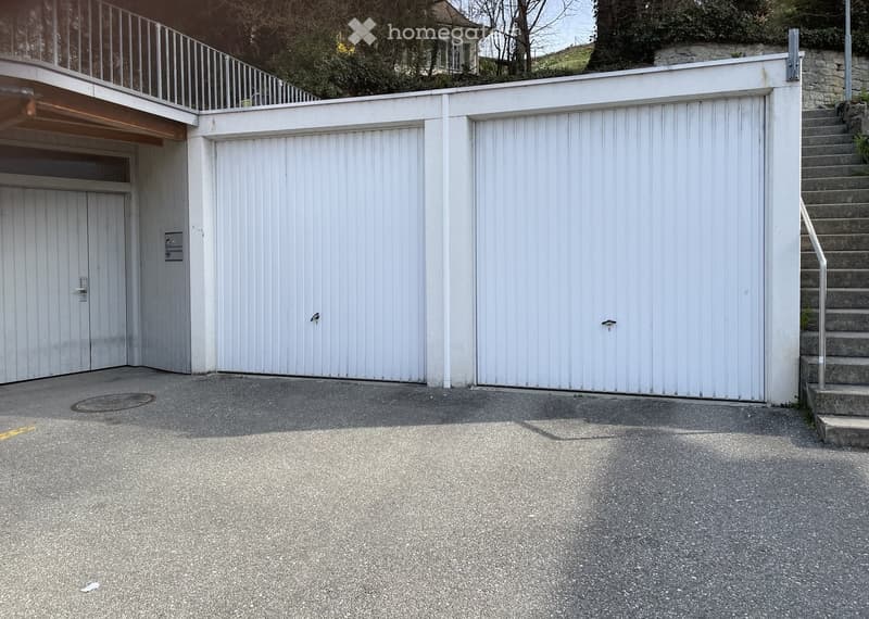 Closed garages, stairs leading to the upper floor, concrete parking lot