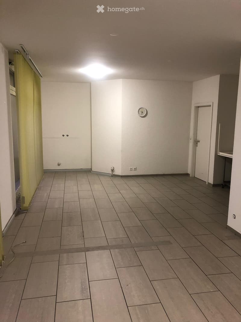 Empty room, tile flooring, white walls, power outlets, door with a clock, yellow curtain.