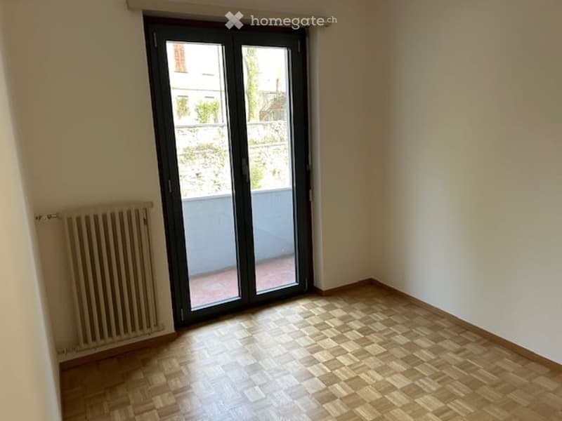 empty room, wooden floors, sliding glass doors leading to a balcony, white walls, wall heater