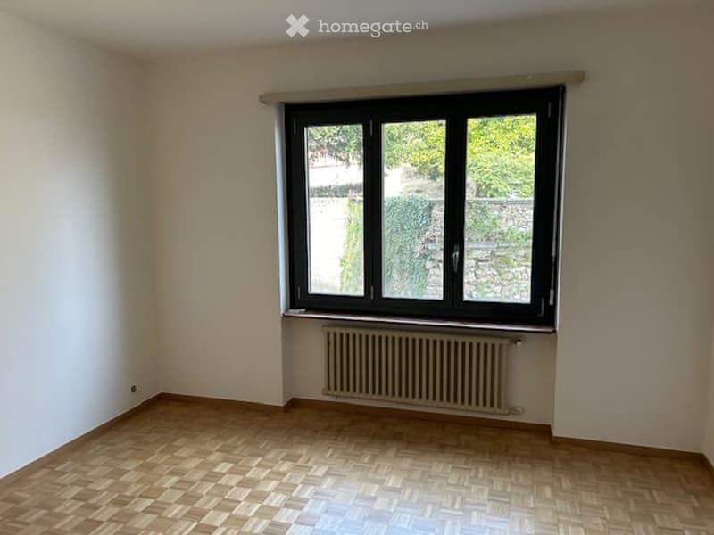Empty room with wooden floor, white walls, a window with a white frame, and a radiator.