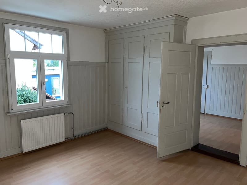white walls, wooden floor, large window, white cabinets