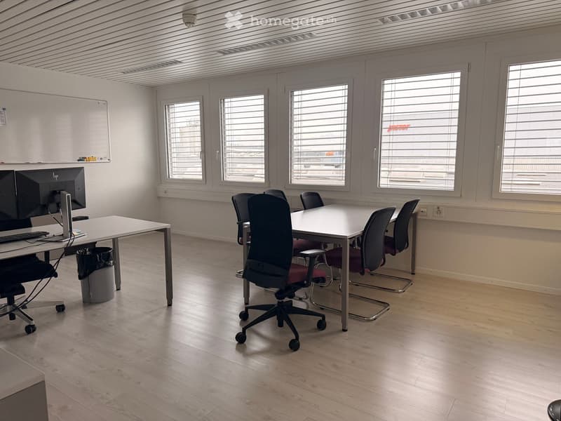 Spacious meeting room with wooden floor, large windows, whiteboard, table, and office chairs.