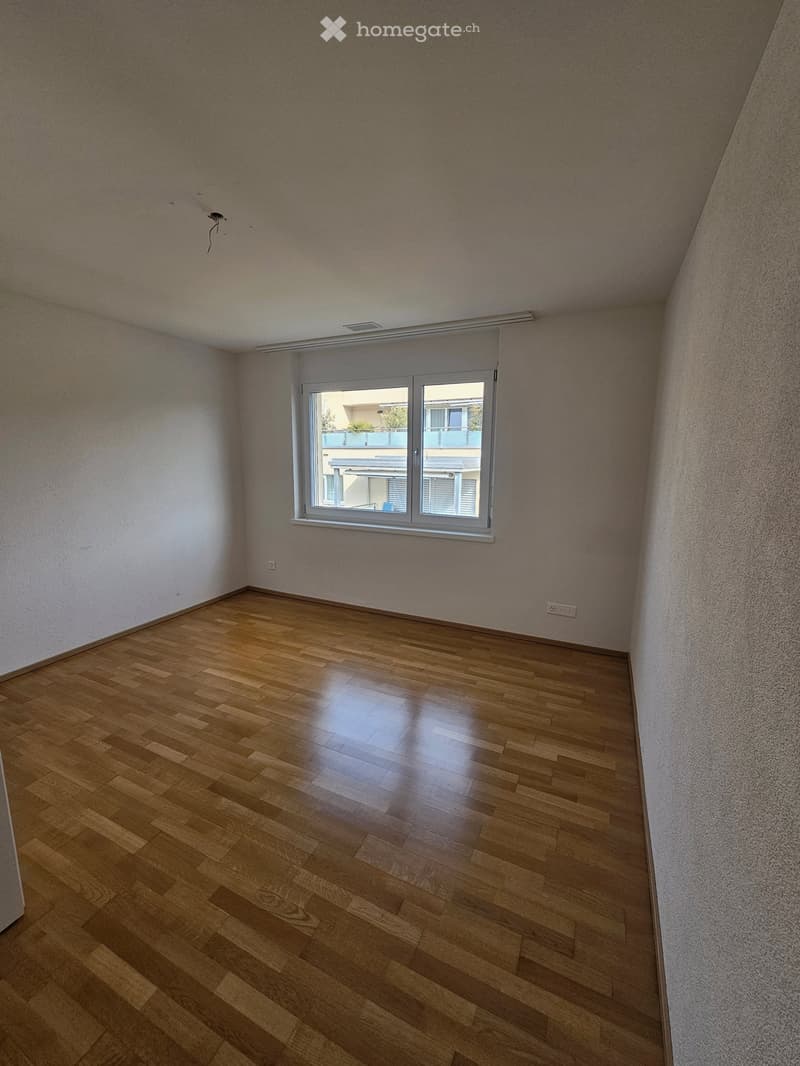 Empty room with white walls, wooden floor, white ceiling, and a window on the right side.