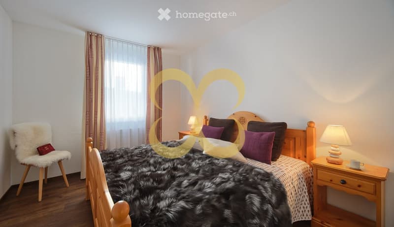 bedroom with wooden bed, fur blanket, pillows, nightstand with lamp, armchair, window with curtains