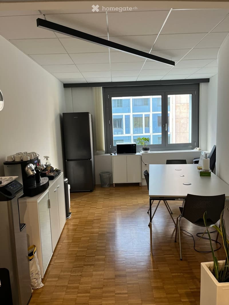 office room with tables, chairs, refrigerator, cabinets, microwave, coffee machine, trash bin, windows, blue building in the distance