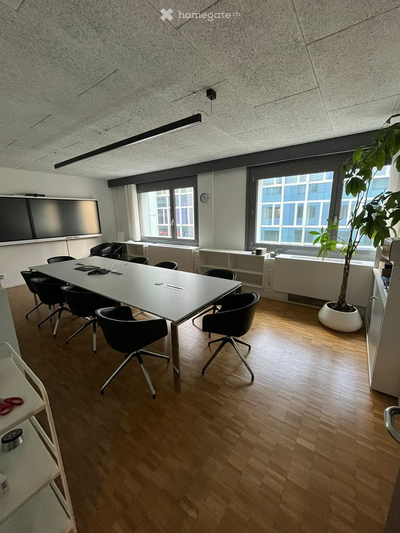 Meeting room, long white table, black chairs, windows, shelf, monitor, small clock