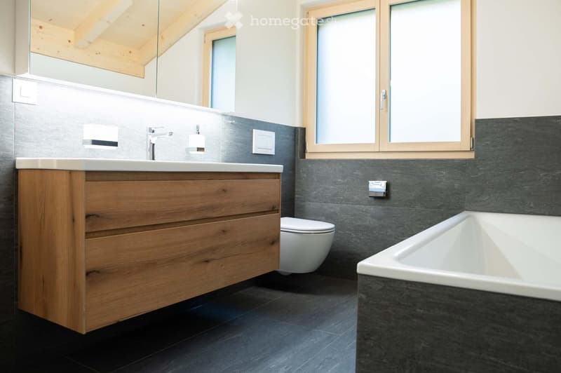 Modern bathroom with a wooden cabinet, white toilet, bathtub, and a large mirror above the sink