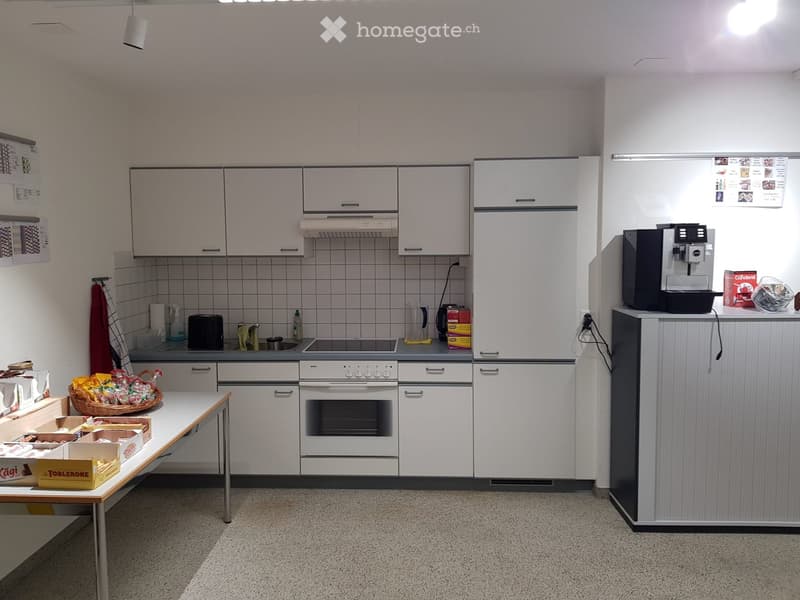 Open plan kitchen with white cabinetry, gas stove, and refrigerator. Includes a coffee machine, food on table.