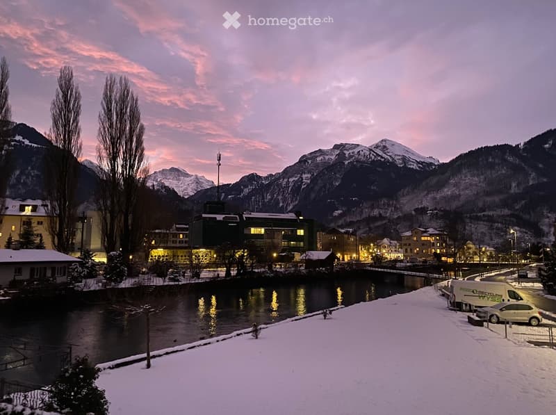 snowy landscape with mountains, river, buildings, and illuminated lights