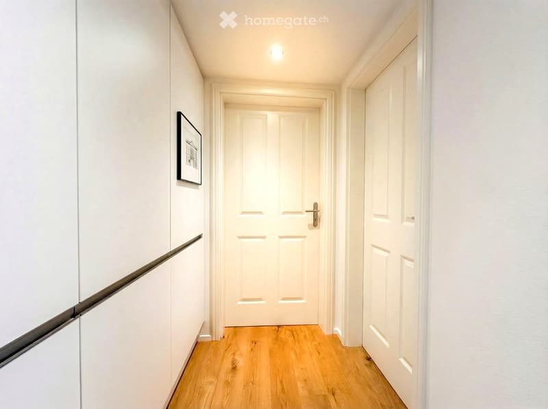 clean hallway with white walls and wooden floor, white doors, picture frame on the wall
