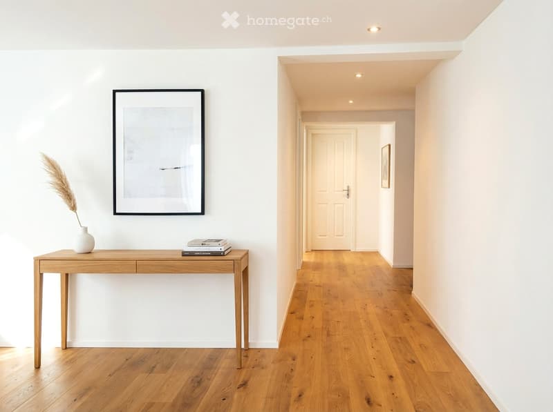 Entrance hallway with wooden floor, white walls, modern frame, vase with flowers, books on the table