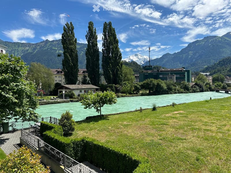 wide green area, river, trees, mountains, house with bridge