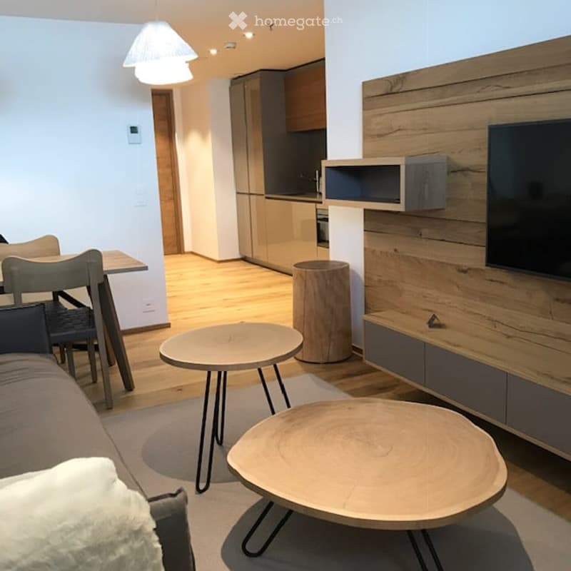 Contemporary open-plan living room, white walls, wooden floor, wooden coffee tables, flatscreen TV, dining table with chairs, and a couch with pillow