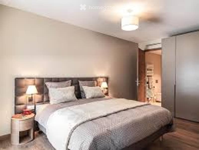 Wooden floor, wall paintings, a bed with grey sheets and pillows, lamps, night tables, a wardrobe with a mirror