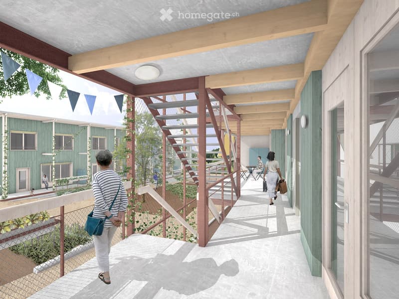 Open corridor, raised ground floor, green walls, wooden beams, stairs, flagpoles with flags, a small garden, and a table with chairs in a green area