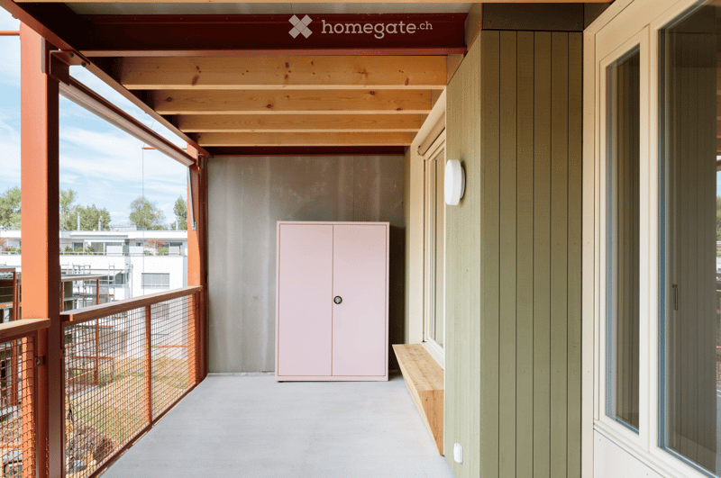 Balcony with wooden ceiling, metal railing, pink cabinet, and bench.
