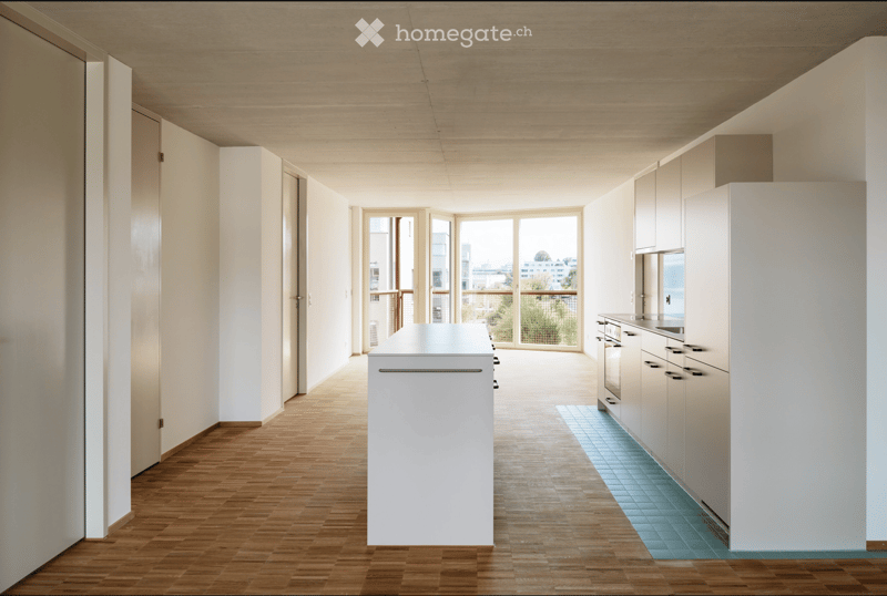 Modern kitchen with white cabinets, a central island, and a sink area. The space features wooden flooring and large windows leading to a balcony.