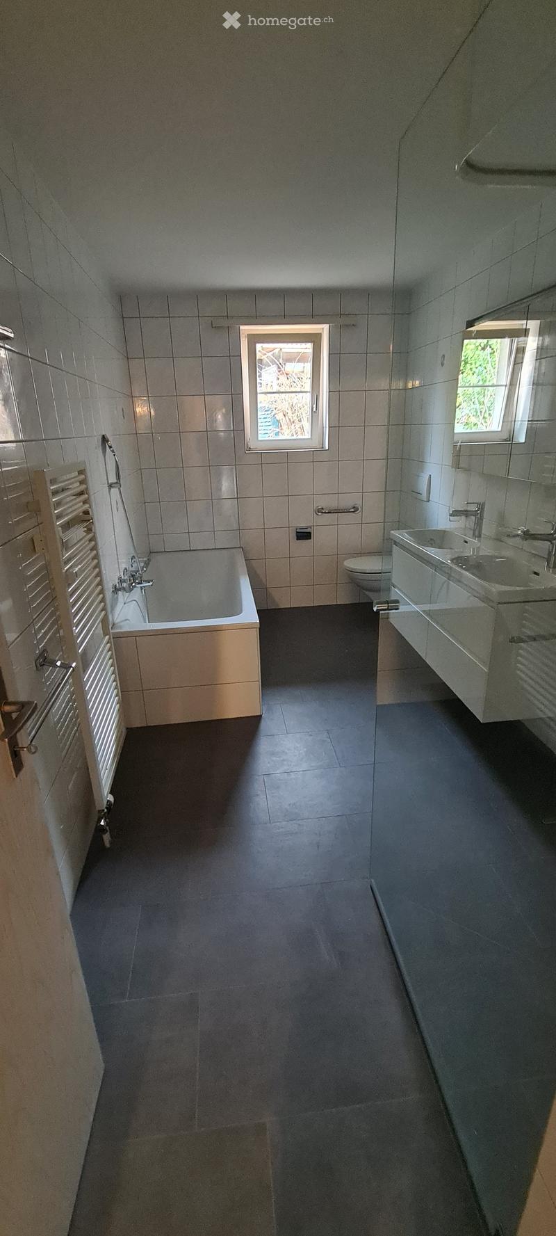 modern bathroom with bathtub, separate toilet, two sinks, wall mounted heating, windows