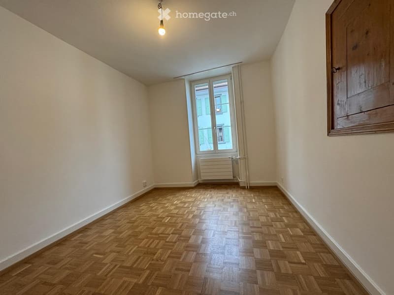 Wooden parquet floor, white walls, large window with shutters, ceiling lamp, radiator