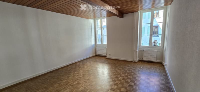 an empty room with wooden floors, white walls, 2 windows with white window frames, white ceiling, and white radiators