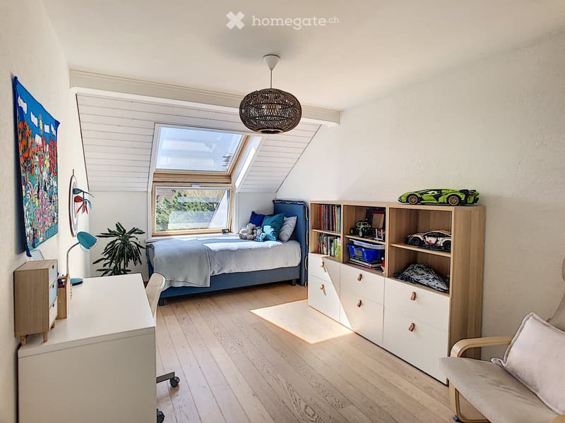 wooden bed, white walls, wood floor, ceiling with skylight, wooden wardrobe with drawers, desk with chair, lamp, plant, bookshelf with toys